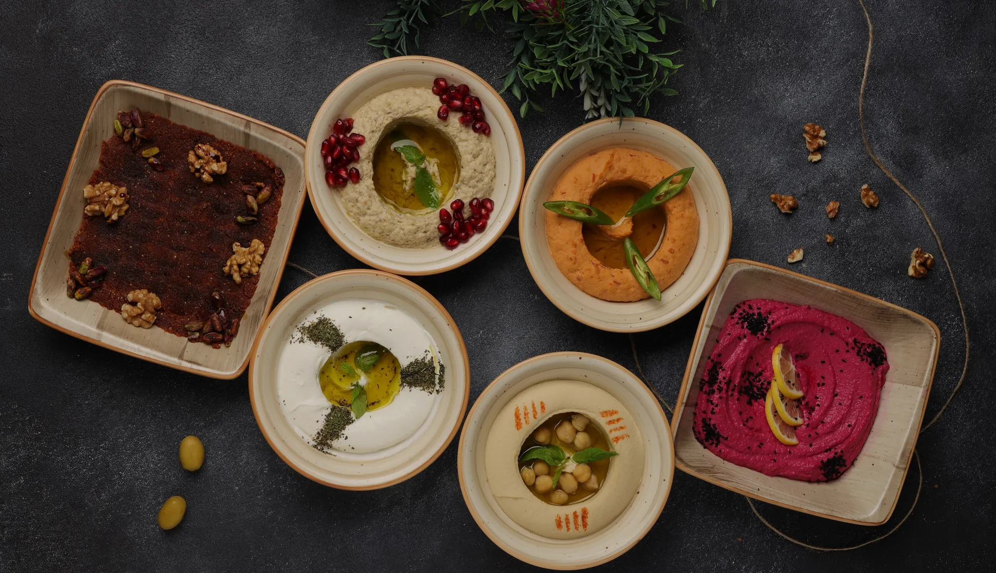 Bowls of hummus, mutabbal, muhammara and other dips on a dark stone table