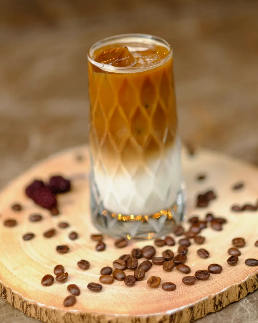 A layered iced latte on a wooden board with coffee beans and dates