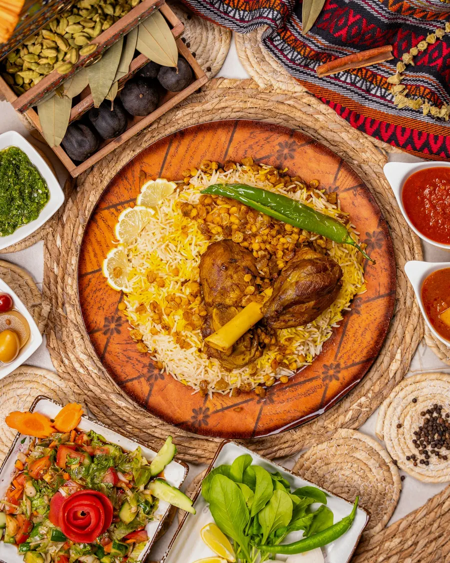 Kabsa rice topped with a lamb shank and green chilli, with salads and sauces around it