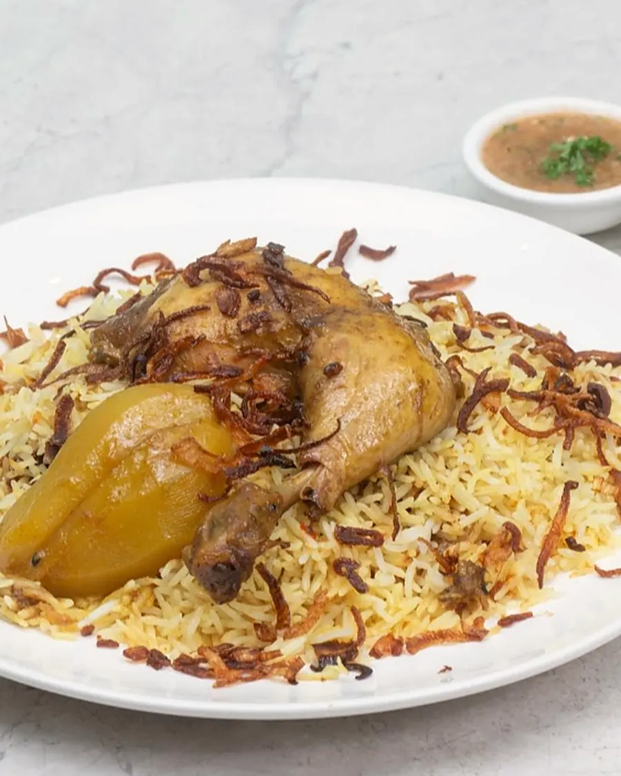 Chicken mandi topped with fried onions on a white plate